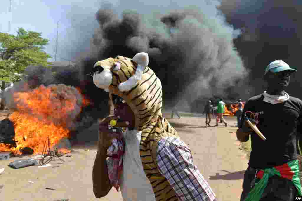 Protesters stand outside the parliament as cars and documents burn outside, in Ouagadougou, Burkina Faso, Oct. 30, 2014.