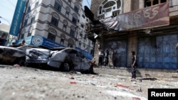 People stand next to damaged cars on a street where Houthi fighters recently clashed with forces loyal to Yemen's former president Ali Abdullah Saleh in Sanaa, Yemen Dec. 5, 2017.