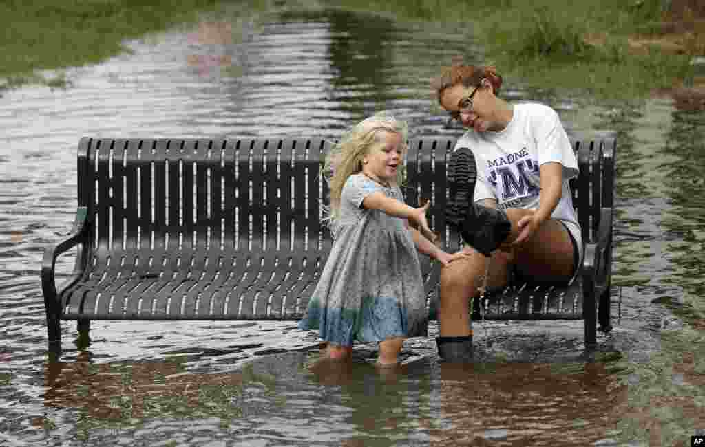 Katie Bender dibantu Johanna Bender (kiri) membuang air dari sepatu bootnya sambil duduk di jalan yang tergenang banjir setelah badai Arthur melewati Manteo, North Carolina. 