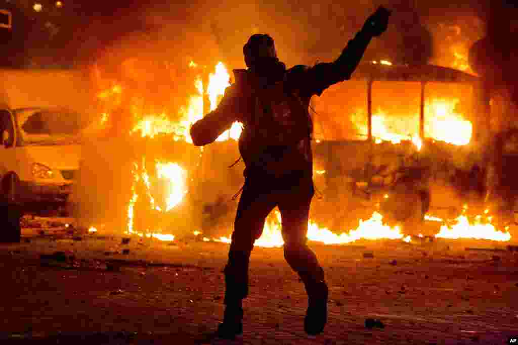 A protester throws a stone towards a burning police bus during clashes with police in central Kyiv, Jan. 19, 2014.