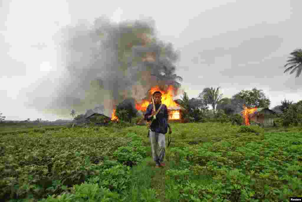 An ethnic Rakhine man holds homemade weapons as he walks in front of houses that were burnt during fighting between Buddhist Rakhine and Muslim Rohingya communities in Sittwe, June 10, 2012.