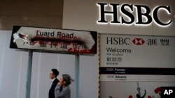 People walk by a vandalized road sign near a HSBC Bank branch covered by panels after damaged by pro-democracy protesters in Hong Kong, Jan. 4, 2020.