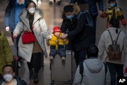 FILE - A man pushes a child riding on a suitcase at Beijing West Railway Station in Beijing, Wednesday, Jan. 18, 2023. (AP Photo/Mark Schiefelbein)