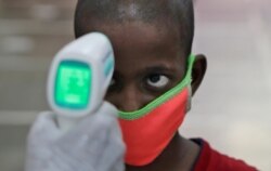 A health worker checks the body temperature of a boy at a medical camp to screen residents for COVID-19 symptoms in Mumbai, India, July 17, 2020.