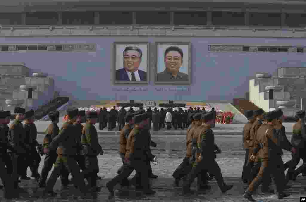 North Korean soldiers march on Kim Il Sung Square in Pyongyang as others pay their respects beneath portraits of the late leaders Kim Jong Il, right, and Kim Il Sung, Dec. 17, 2013.