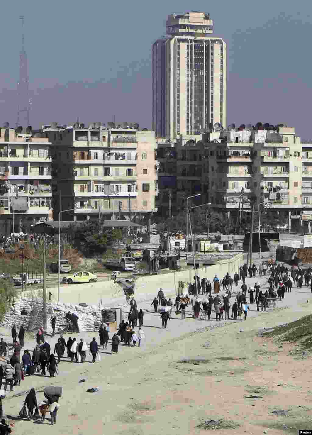 Civilians carry their belongings as they walk at the Karaj al-Hajez crossing, a passageway separating the Bustan al-Qasr district, which is under the rebels' control and the Al-Masharqa district, an area controlled by the Assad regime, Aleppo, Feb. 9, 2014. 