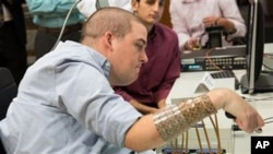 In this March 2016 photo provided by Ohio State University, Ian Burkhart plays a guitar video game as part of a study with neural bypass technology at The Ohio State University Wexner Medical Center in Columbus. A computer chip in Burkhart's brain reads h