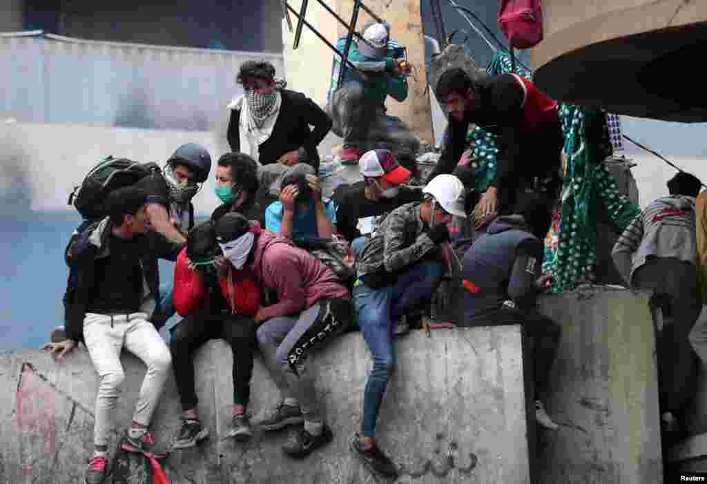 عراقی دارالحکومت بغداد میں مظاہرین پولیس کی جانب سے استعمال کی جانے والی آنسو گیس سے بچنے کوشش میں ایک دیوار پر بیٹھے ہیں۔ 