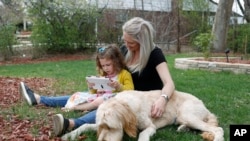 Katie Evers, who is facing the specter of paying the monthly rent with the flip of the calendar, helps her 4-year-old daughter, Everlee, read a tablet while their goldendoodle lies next to them outside their home in southeast Denver, April 30, 2020.