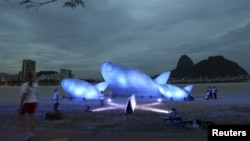 Seorang wanita melintasi ikan raksasa yang terbuat dari botol plastik dan dipamerkan di Pantai Botafogo, Rio de Jenairo (19/6). Konferensi Pembangunan yang Berkelanjutan PBB Rio +20 akan berlangsung di kota ini dari tanggal 20 hingga 22 Juni 2012.