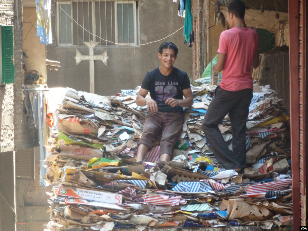 Para pemuda Kristen Koptik di antara tumpukan lipatan kardus di daerah Manshiyat Naser, atau 'Kota Sampah' di Kairo (18/7). (VOA/S. Behn)