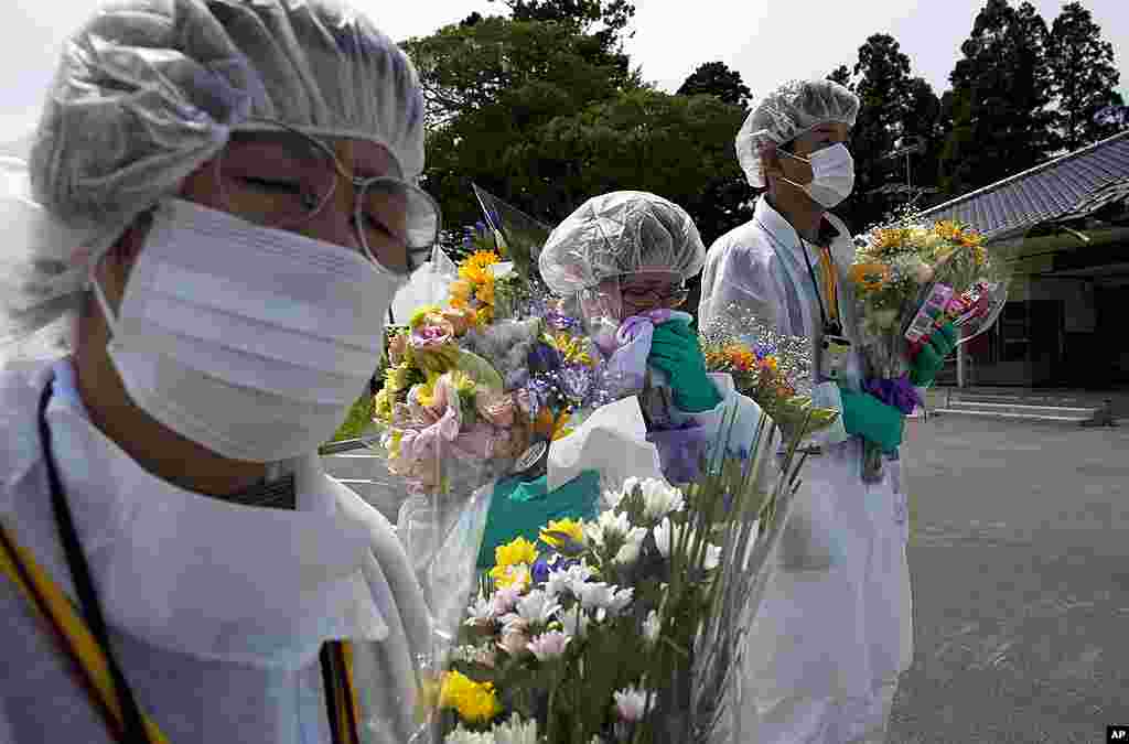 Warga yang berduka cita memakai pakaian pelindung dan memegang bunga pada upacara peringatan bagi penduduk kota Okuma, dekat PLTN Fukushima, 24 Juli 2011.