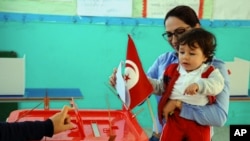 Une femme vote avec son enfant lors du premier tour de l'élection présidentielle tunisienne dans un bureau de vote à Marsa, à l'extérieur de Tunis, le 23 novembre 2014.