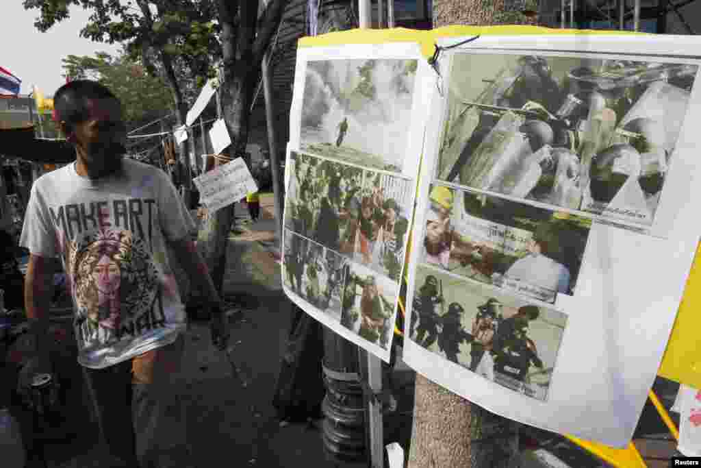An anti-government protester walks past pictures taken during clashes with riot policemen during a rally outside the Government House in Bangkok, Thailand, Dec. 29, 2013.