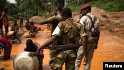 FILE - Former Seleka soldiers look at prospectors as they pan for gold near the open pit at the Ndassima gold mine in the Central African Republic, May 9, 2014.