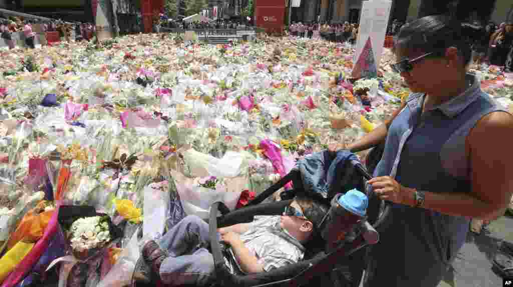 Seorang ibu dan anaknya melewati situs memorial dekat kafe Lindt di distrik bisnis Sydney, Australia, tempat warga terus memberikan bunga tanda penghormatan, Kamis (18/12). (AP/Rob Griffith)