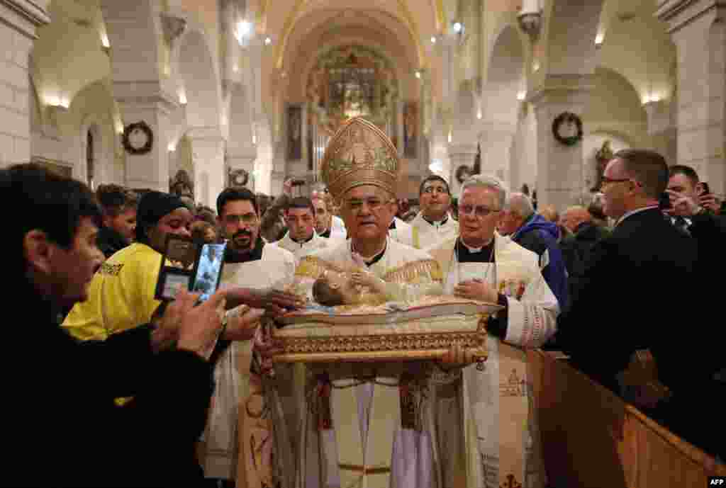 Pemimpin kelompok agama Kristen Patriarki di Yerusalem, Fouad Twal (tengah) membawa patung bayi Yesus dalam misa tengah malam Natal di Gereja Nativity, yang diyakini sebagai tempat kelahiran Yesus Kristus, di kota Alkitab Bethlehem, Tepi Barat (25/12).