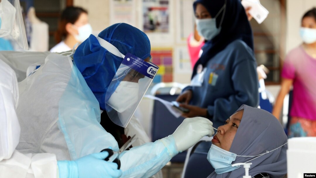 FILE - A medical worker collects a swab sample from a Top Glove worker to be tested for the COVID-19 outside a hostel under enhanced lockdown in Klang, Malaysia, Nov. 18, 2020. 