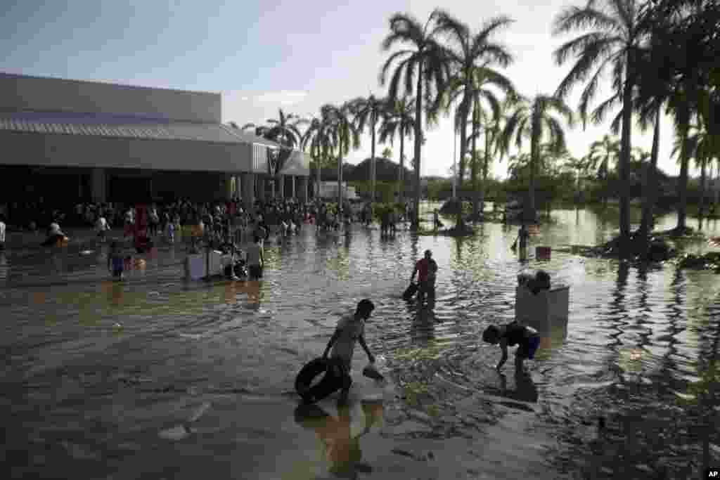 People wade through waist-high water in a store's parking, looking for valuables, south of Acapulco, in Punta Diamante, Mexico, Sept. 18, 2013.