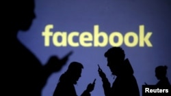 FILE PHOTO: Silhouettes of mobile users are seen next to a screen projection of Facebook logo in this picture illustration taken March 28, 2018.