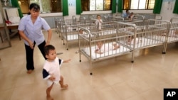 In this 2007 file photo, a staff member follows an orphan at the Tam Binh 1 Orphanage in Ho Chi Minh City.