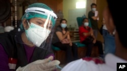 Seorang nakes memberikan suntikan vaksinasi COVID-19 produksi AstraZeneca dalam program vaksinasi massal di Denpasar, Bali, 22 Maret 2021. (AP Photo/Firdia Lisnawati)