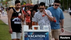 Hombres jóvenes leen las precauciones de seguridad pública mientras disfrutan de los bares y restaurantes en South Beach durante las vacaciones de primavera en medio de la pandemia del coronavirus, en Miami, el 27 de marzo de 2021.