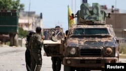 Kurdish fighters from the People's Protection Units (YPG) stand near a military vehilce in the southeast of Qamishli city, Syria, April 22, 2016.
