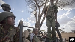 A Kenyan army soldier, left, looks up as a Somali government soldier, right, climbs across the vehicle that they are sharing, and another Somali government soldier prepares to drive, center, in Tabda, inside Somalia, February 20, 2012.