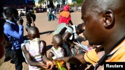 Mtu akiwapa watu vitakasa mikono kabla ya abiria hao kupanda basi akiwa ni hatua ya kudhibiti kuenea kwa virusi vya corona katika kituo cha mabasi cha zamani, Kampala, Uganda Machi 24, 2020. REUTERS/Abubaker Lubowa 