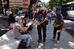 Juan Pablo Lares distributes free copies of a newspaper "Enterate" to people at a bus stop in Caracas, Venezuela, Saturday, July 31, 2021. (AP Photo/Ariana Cubillos)