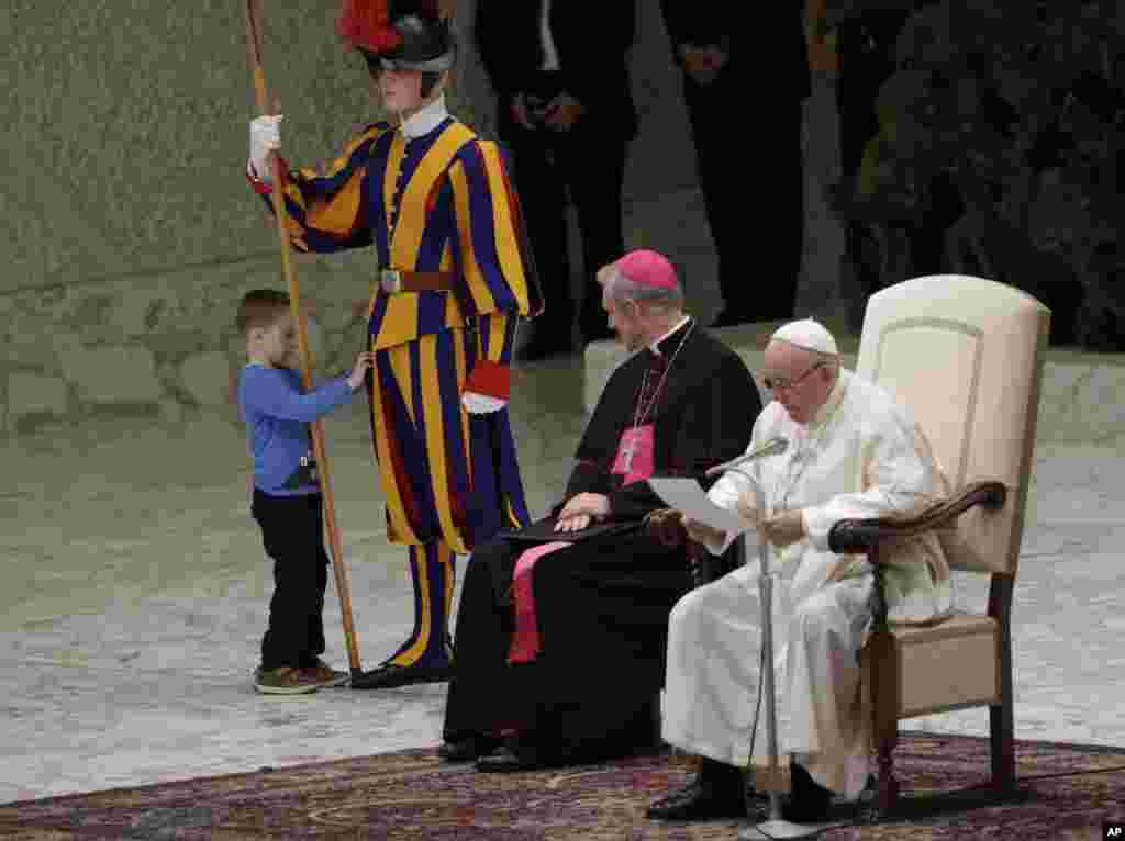 A child plays with a guard while the pope gives an address at the Paul VI Hall at the Vatican.