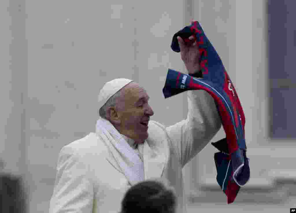Pope Francis grabs a shirt thrown to him by faithful as he leaves at the end of his weekly general audience in St. Peter's Square at the Vatican.