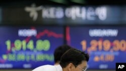 A currency trader watches the computer monitors near the screens showing KOSPI, left, and the foreign exchange rate between the U.S. dollar and South Korean won at the foreign exchange dealing room in Seoul, South Korea, Aug. 6, 2019.