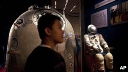 In this July 6, 2011 photo, a visitor stands near the Shenzhou 5 re-entry capsule, that was used in China's first human spaceflight mission, and the the space suit worn by crew member Yang Liwei at an exhibition in Beijing, China.
