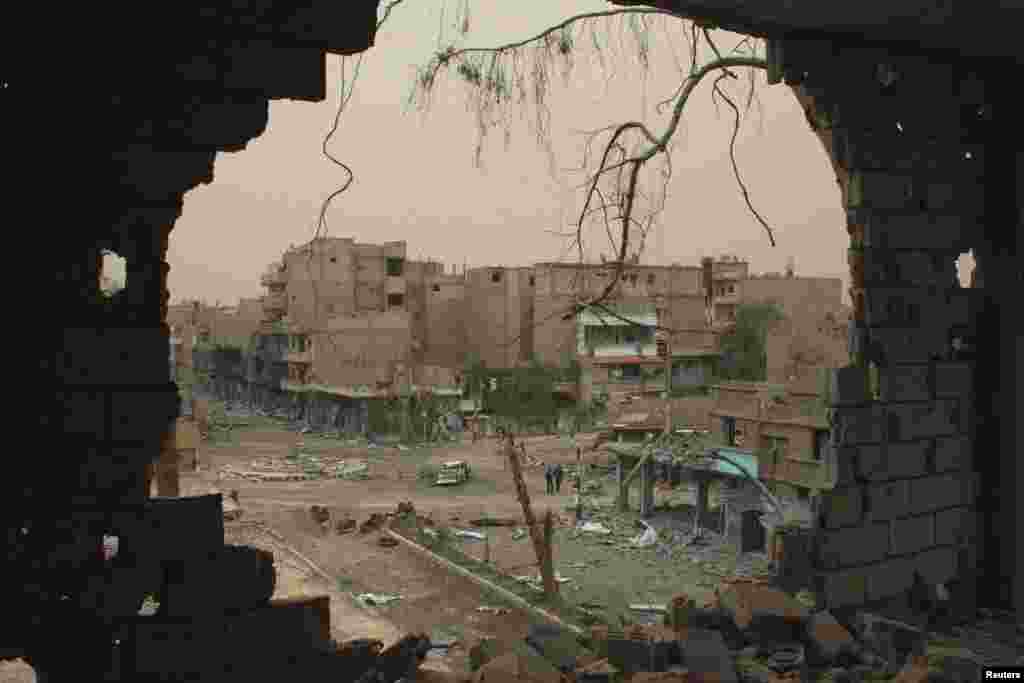 People walking down a street are pictured through a hole in a building in Deir al-Zor, Syria, April 4, 2013.