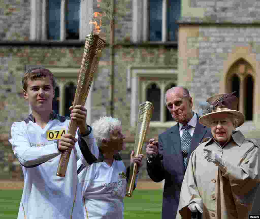 Britain's Queen Elizabeth (R), Prince Philip (2nd R), and Olympic torch bearer Gina Macgregor (2nd L) watch as torchbearer Phil Wells takes the Olympic Flame at Windsor Castle, west of London July 10, 2012.