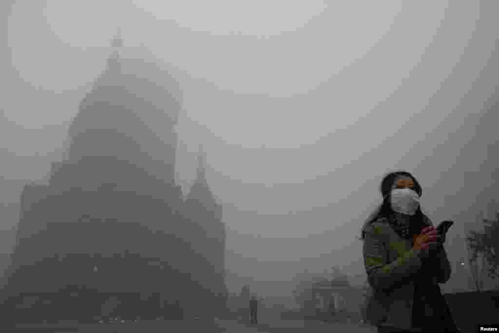 A woman wearing a mask checks her mobile phone during a smoggy day on the square in front of Harbin's landmark San Sophia church, China, Oct. 21, 2013.