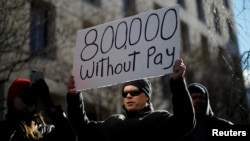 FILE - A demonstrator holds a sign, signifying hundreds of thousands of federal employees who won’t be receiving their paychecks as a result of the partial government shutdown, during a “Rally to End the Shutdown” in Washington, Jan. 10, 2019.