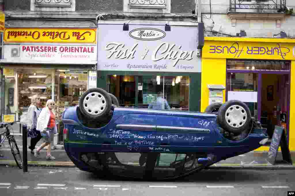 A car is seen parked on its roof in front of shops with upside down signs in a street of Nantes, western France, as part of the "A journey to Nantes" (Le Voyage a Nantes) art festival.