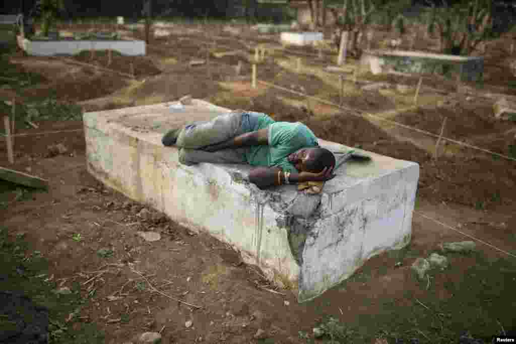 Un fossoyeur s’en dort sur une tombe près de l’endroit où des victimes d'Ebola sont enterrées dans un cimetière de Freetown, 17 décembre 2014. REUTERS / Baz Ratner