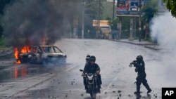 FILE - A police officer aims his shotgun at two men riding a motorcycle during a protest against Nicaragua's President Daniel Ortega in Managua, Nicaragua, May 28, 2018. 