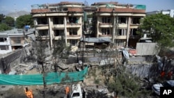 FILE - Afghan municipality workers clean debris in front of the damaged buildings a day after Taliban fighters attacked the offices of a U.-based aid organization in Kabul, May 9, 2019