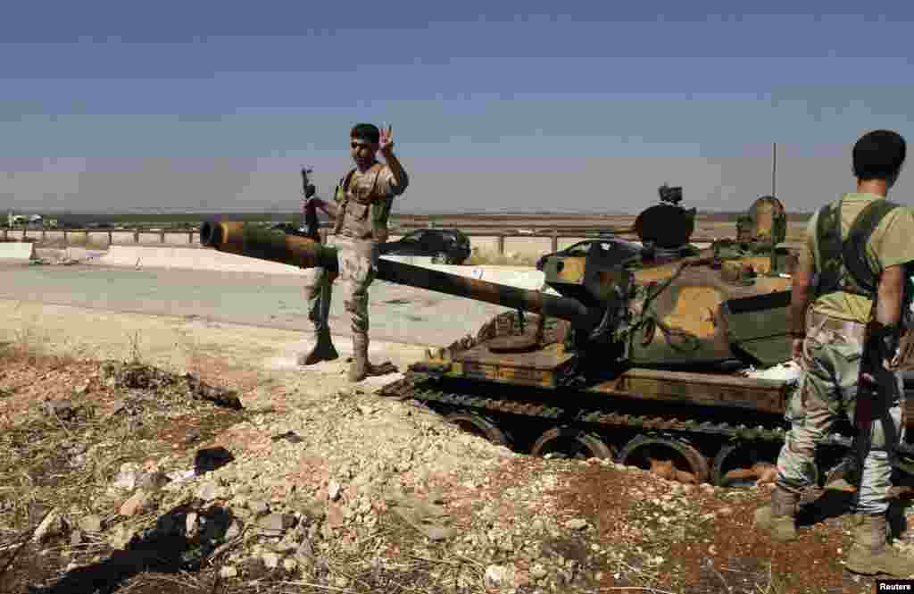 A Free Syrian Army fighter flashes a victory sign as he poses for a picture atop of a damaged tank that belongs to forces loyal to Syria's President Bashar al-Assad, outside the Minnig Military Airport, August 6, 2013.