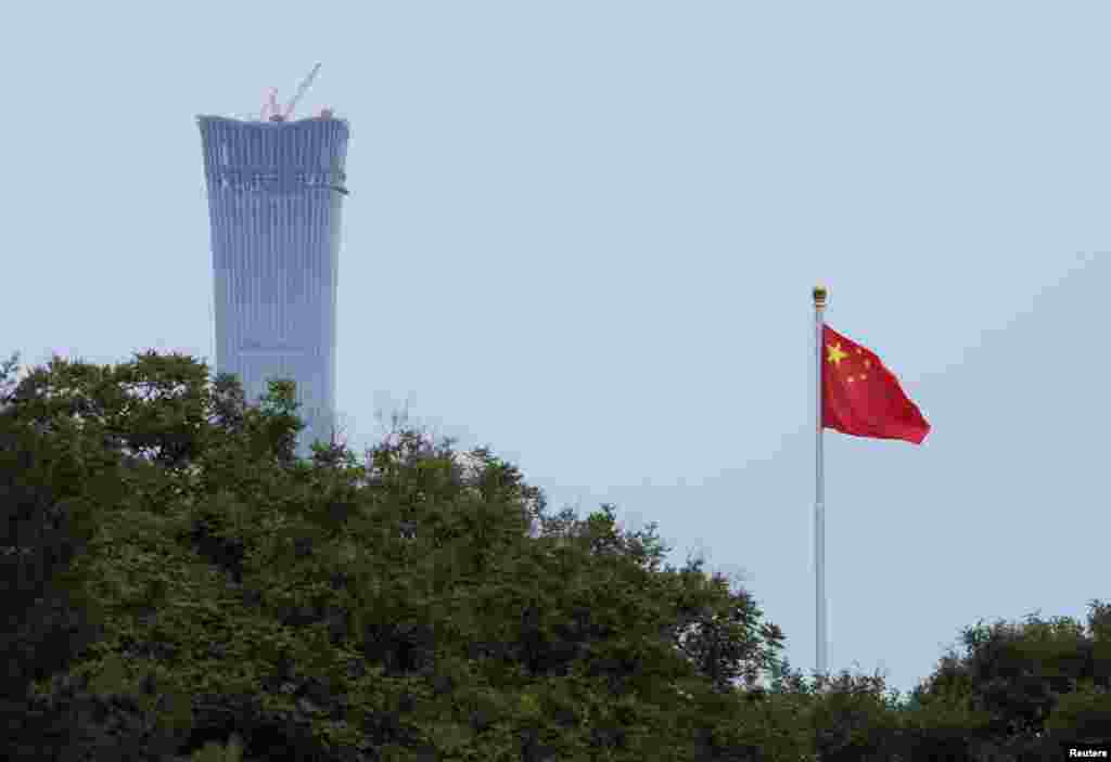 2018年6月8日,北京市中心的天安门广场飘扬着国旗。照片上的大楼是正在施工的“中国尊”,计划成为北京最高的建筑。这是中信集团总部大楼,位于北京市商务中心区。中国尊的名字来自中国古代的盛酒器皿“尊”。