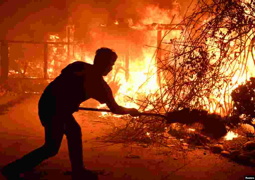Home owner Will Buckley uses a shovel with dirt to try to stop the flames from from destroying a neighbor's home during the Woolsey Fire in Malibu, California, Nov. 9, 2018.