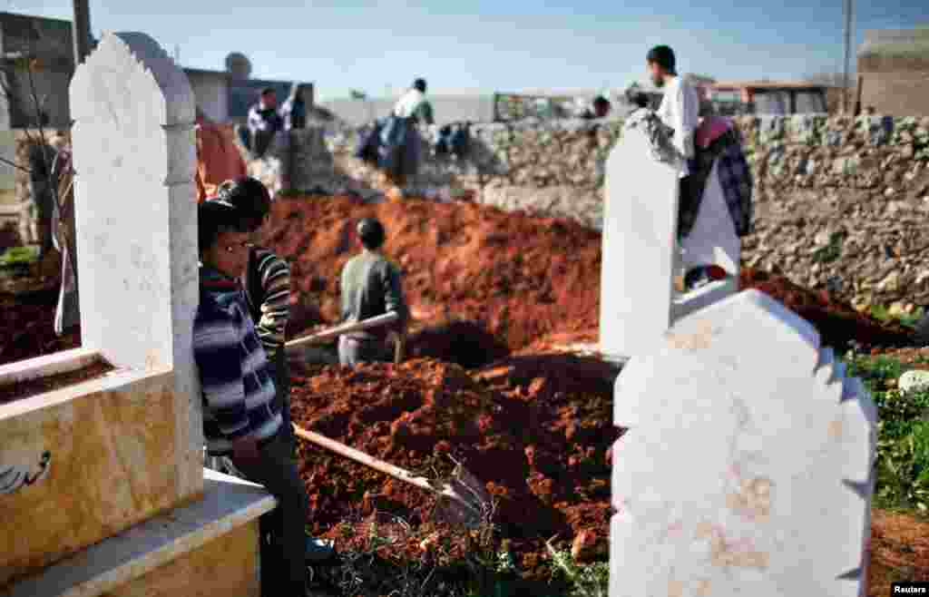 A boy watches men dig graves for future casualties of Syria's civil conflict at Sheikh Saeed cemetery in Azaz city, December 30, 2012.