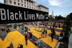 FILE - A street sign of Black Lives Matter Plaza and giant yellow letters spelling "Black Lives Matter" on the street are seen near St. John's Episcopal Church, in Washington, June 5, 2020.