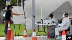 Health care workers take information from people in line at a walk-up COVID-19 testing site during the coronavirus pandemic, July 17, 2020, in Miami Beach, Fla. 