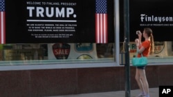 Seorang wanita memotret poster penyambutan Presiden AS, Donald Trump, dan Presiden Rusia, Vladimir Putin, di sebuah toko di pusat kota Helsinki, 14 Juli 2018 (foto: AP Photo/Markus Schreiber)